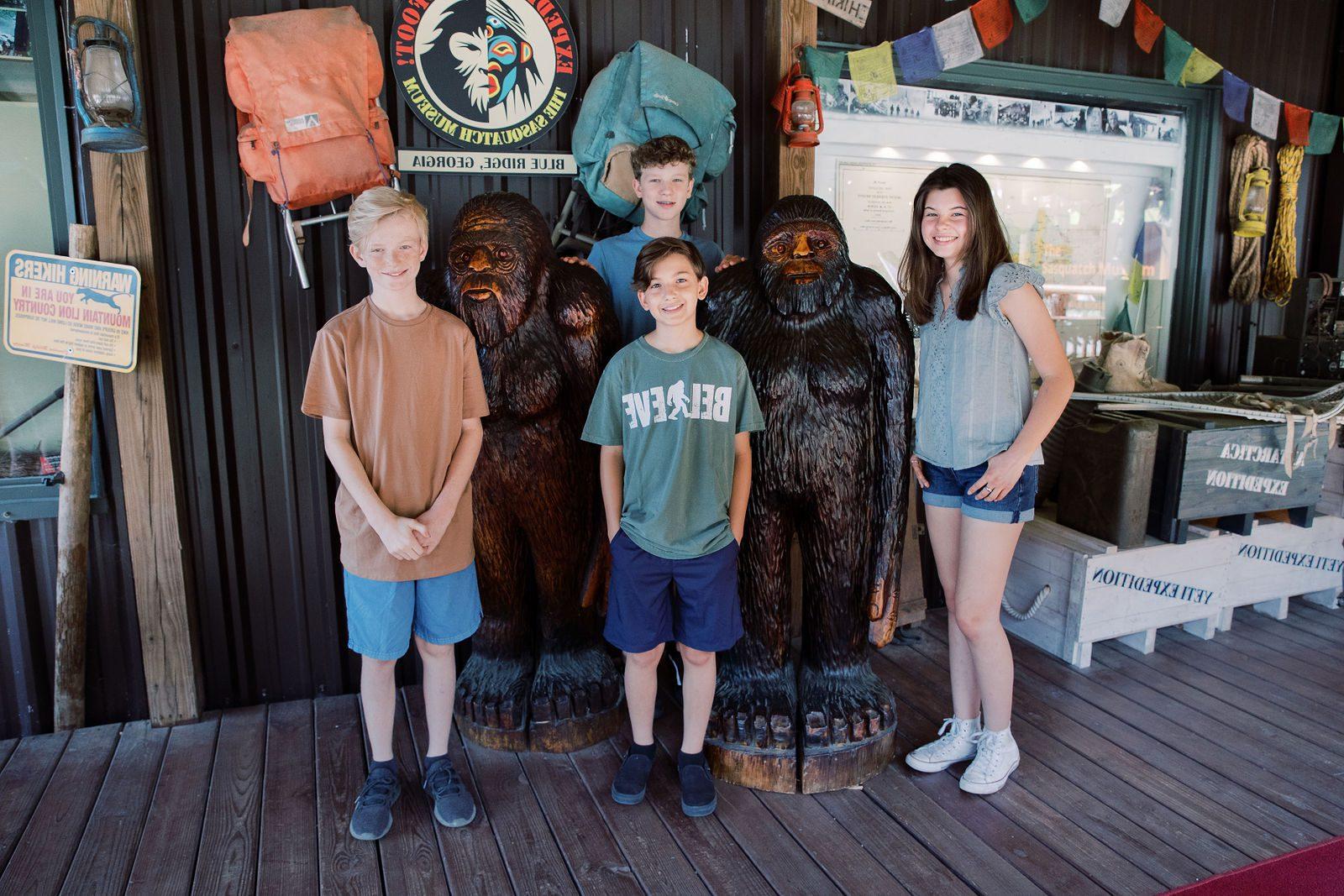 children standing next to carved statues of Bigfoot